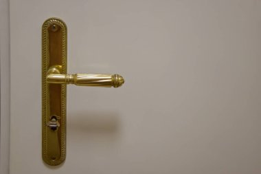 Beyaz kapıdaki klasik altın kapı kolunun yakın plan görüntüsü. Kapı kolu karmaşık detaylar ve klasik bir tasarım içeriyor, kapıya zarafet katıyor..