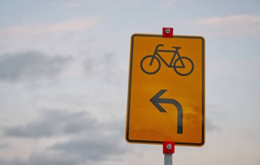 Bisikletler için sola dönüş gösteren sarı bir trafik işareti, bisiklet simgesi içeriyor.