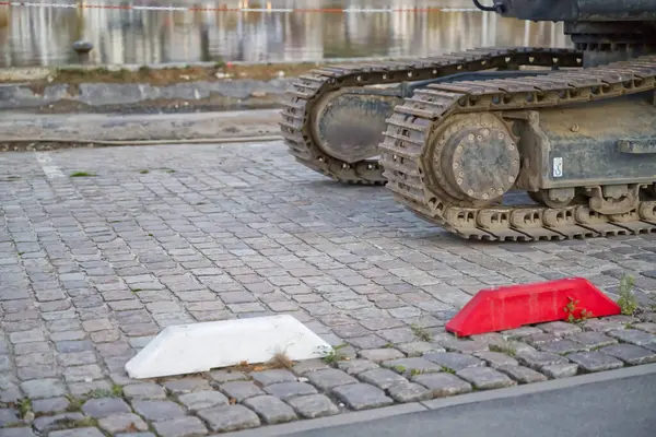 Yakınlarda kırmızı ve beyaz trafik bariyerleri olan kaldırım taşları üzerindeki bir tankın izlerini yakından takip edin. Olay yeri askeri ekipmanları kentsel bir ortamda yakalıyor..