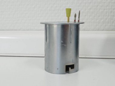 Düz tepeli metalik silindirik bir nesne, sarı plastik uçlu ve içinden çıkan iki metal prob içeriyor. Nesne, muhtemelen elektrik veya mekanik uygulamalarda kullanılan bir araç veya aygıt gibi görünüyor..