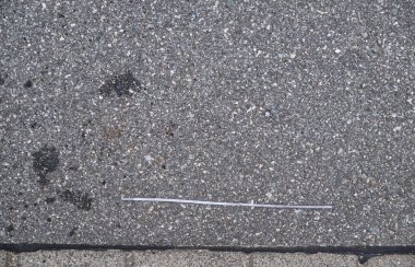 İnce, düz bir plastik ya da metal parçası dokulu asfalt bir yüzeyde, etrafında küçük taşlar ve kir var..