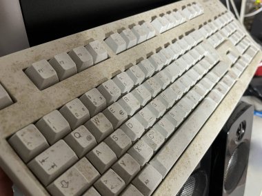 Eski, tozlu, yıpranmış tuşları olan bir bilgisayar klavyesinin yakın çekim görüntüsü. Klavye, kirli yüzeyini ve solmuş harflerini gösteren bir açıyla konumlandırılmış..