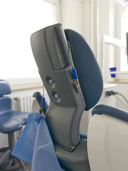 Mavi yastıklı ve ayarlanabilir başlıklı bir diş sandalyesinin yakın görüntüsü. Sandalye parlak bir diş muayenehanesinde, arka planda modern diş aletleri sergileniyor..