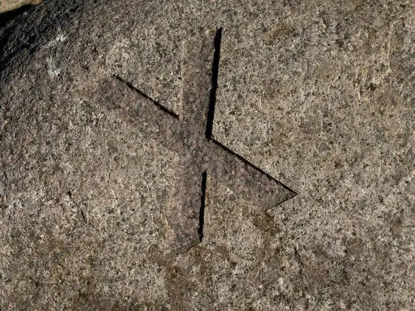 Yüzeye kazınmış belirgin bir haç şeklindeki oyulmuş bir taşın yakın çekim görüntüsü. Taşın yapısı pürüzlü ve doğal, oyulmuş bölge ile etrafındaki kaya arasındaki zıtlığı vurguluyor..