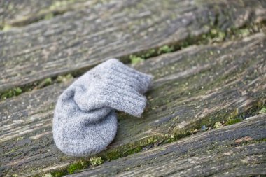 Yıpranmış ahşap bir yüzeyde uzanan tek bir gri çorap çorap, doğal doku ve renklerle çevrili..