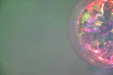 Yumuşak, bulanık bir arka planı olan renkli, yansıtıcı bir kürenin yakın çekimi. Küre canlı renkler ve ışık yansımalarının bir karışımını göstererek rüya gibi bir etki yaratıyor..