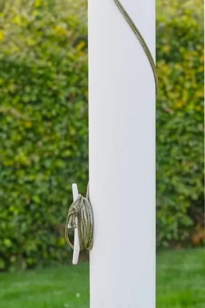 Çevresine yeşil bir ip bağlanmış beyaz bir direğin yakın-p 'si, bulanık yeşil bir çit arka plan üzerine kurulmuş.