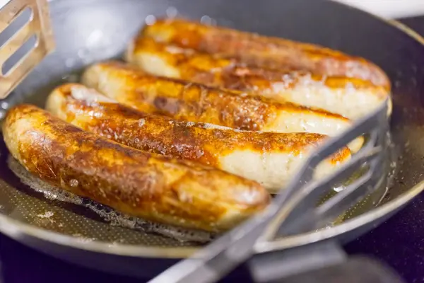 Kızartma tavasında cızırdayan sosislerin yakın çekim görüntüsü altın-kahverengi, kıtır kıtır dış görünüşlerini gözler önüne seriyor. Tava yapışmaz ve biraz da yağ var..