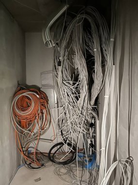 Karışık kablolar ve beyaz ve turuncu da dahil olmak üzere çeşitli renklerde kablolarla dolu dağınık bir oda. Duvarlar boş, zemin de tamamlanmamış. İnşaat ya da yenileme alanı olduğunu gösteriyor..