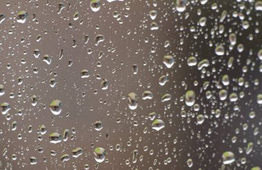 Penceredeki yağmur damlalarının yakın plan görüntüsü bulanık bir arka plan etkisi yaratıyor. Damlacıkların boyutları değişir ve ışığı yansıtarak yağmurlu atmosferi güçlendirirler..