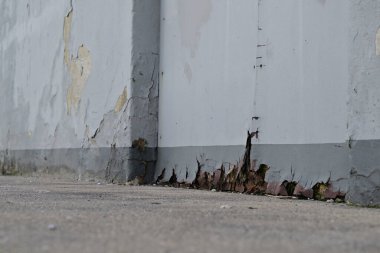 Yıpranmış bir duvara yakın plan, çift katlı bir kapı, soyulmuş boya ve nem hasarı ve tabanda çatlaklar, ihmal ve yaşlanma belirtileri gösteriyor..