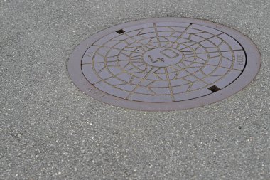 Gri asfalt bir yola yerleştirilmiş yuvarlak bir rögar kapağı, geometrik desenli ve üzerine 40 numara kazınmış..