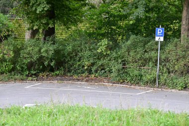 Ağaçlar ve çalılarla çevrili yeşil bir alanda boş bir park yeri. Yakınlarda park yeri tabelası var. Bu da uzayın amacını gösteriyor..