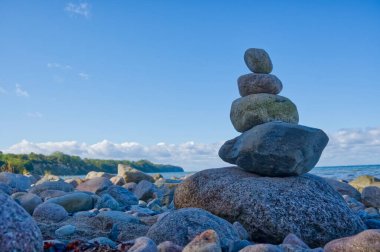 Huzurlu bir sahil sahnesi. Kayalık bir sahilde kayalık taşlar yığını. Arka planda okyanus ve mavi gökyüzü..