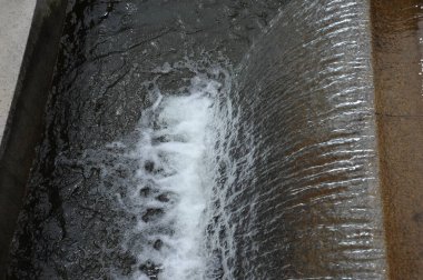 Taştan bir kenarda akan suyun yakın çekim görüntüsü, dingin bir ortamda dalgalanmalar ve kabarcıklar yaratır..