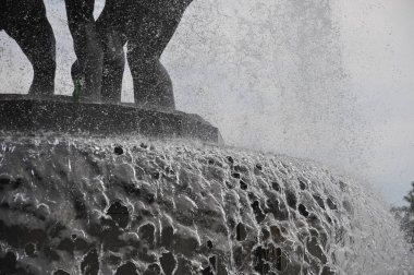 Bir fıskiyenin yakın plan görüntüsü, taştan bir yüzey üzerinde çağlayan su sisli bir etki yaratıyor. Görüntü, suyun dinamik hareketini ve taşın dokusunu yakalar..