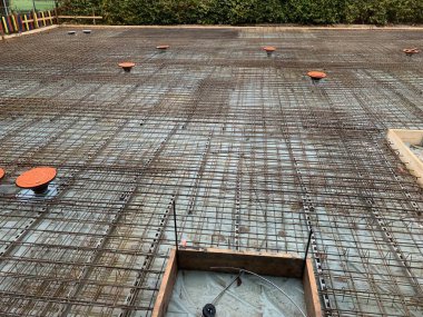 Çelik inşaat ızgarası ve drenaj boruları olan büyük beton bir levha. Alan, aralıklarla dairesel biçimlerle beton dökmeye hazır..