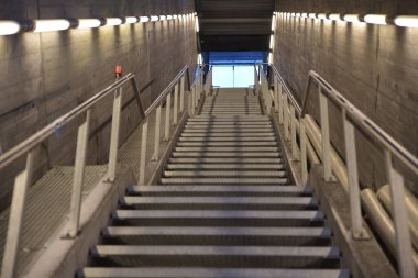 Metal parmaklıkları ve beton bir duvarı olan modern bir merdiven. Doğal ışık tepede görünür, derinlik ve perspektif duygusu yaratır..