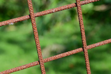 Paslı metal bir ızgaraya yakın çekim, bulanık yeşil bir arka plan, metalin dokusunu ve çürümesini gösteriyor..