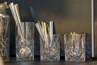 Karanlık bir yüzeyde metal pipetler tutan üç kristal bardak..