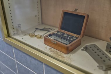 Cam bir kutuda sergilenen ahşap bir kutunun içindeki bir aletin klasik tıbbi veya bilimsel ağırlığı.