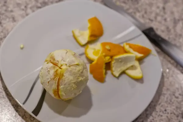 Beyaz bir plaka üzerinde yarı soyulmuş bir portakal ve yanında bir bıçak..