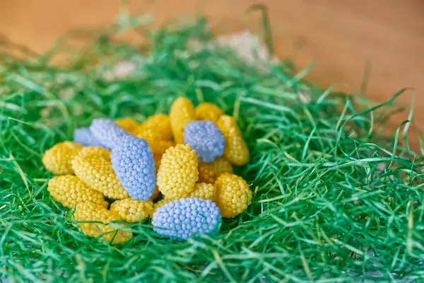 Paskalya yumurtaları ve Paskalya şekerlerinin yanında Ukrayna bayrağı renginde yeşil, çimenimsi bir malzeme var. Şekerler sarı ve mavi ve incili yumurtalar..
