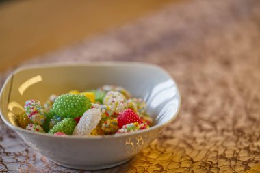 Paskalya yumurtaları ve Paskalya tatlıları çeşitli parlak renklerde altın arka planda beyaz bir porselen kasede yatıyor.