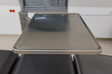 Tıbbi muayene masasındaki paslanmaz çelik tepsinin yakın plan görüntüsü, nötr renklerle modern bir klinik ortamda geçiyor..