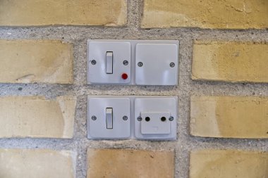 Eski Danimarka elektrik düğmelerinin yakın çekim görüntüsü ve desenli tuğla bir duvara monte edilmiş bir soket. Düğmeler arasında bir anahtar ve kırmızı gösterge ışığı olan bir düğme yer alıyor