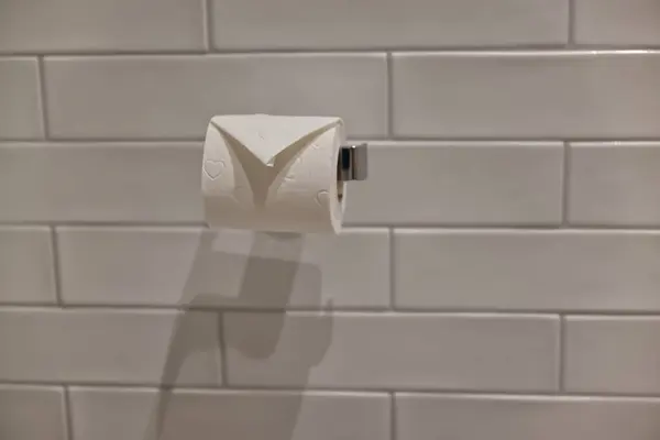 Kiremit kaplı bir duvarda tuvalet kağıdı rulosunun yakın çekim görüntüsü. Rulo kısmen kullanılır, dokusunu ve tasarımını gösterir. Arka planda, temiz ve modern bir banyo estetiği yaratan beyaz metro fayansları yer alıyor..
