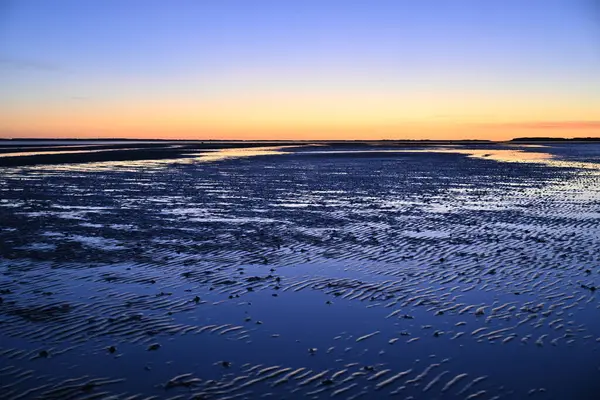 Gün batımında Foehr Adası 'ndaki gelgit düzlüğünün sakin manzarası dalgalanan su desenleri gökyüzünün canlı renklerini yansıtıyor. Ufuk, gece gündüz gibi ılık renklerle parlar..