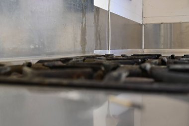 Parlak bir yüzeyi ve metal arka paneli olan bir gaz sobasının yakın çekimi mutfak ortamındaki ocakları ve ızgaraları gösteriyor, önünde bulanık bir kibrit var.