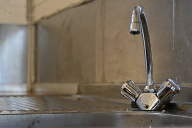 Metalik arka planda iki saplı krom mutfak musluğunun yakın çekim görüntüsü. Musluk parlak ve ışığı yansıtıyor, modern tasarımını sergiliyor..