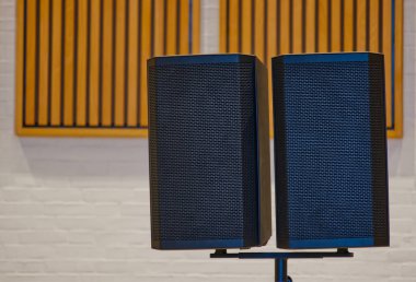 İki siyah ses hoparlörü, ahşap akustik panellerle çevrili. Hoparlörlerin modern bir tasarımı var, müzik etkinlikleri veya stüdyo ayarları için uygun..