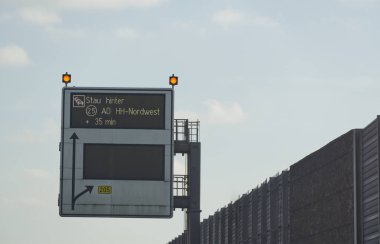 Otobandaki trafik sıkışıklığı uyarısı gösteren bir trafik bilgisi tabelası 35 dakikalık bir gecikmeyi gösteriyor. İşaret, Hamburg yakınlarında açık mavi gökyüzü olan yüksek bir yapıya monte edilmiştir.