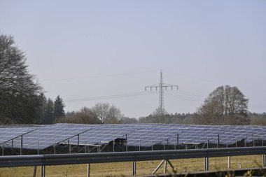 Kiel yakınlarındaki A7 'nin arka plan görüntüsünde ağaçlar ve elektrik hatlarıyla çevrili, berrak bir gökyüzü altında sıra sıra güneş panelleri olan bir güneş çiftliği..