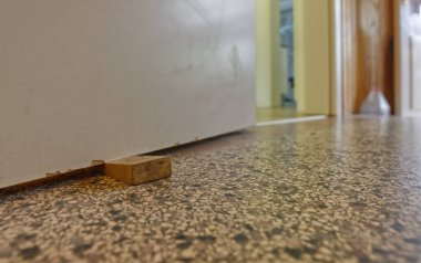 Ahşap bir kapı tutacağının yakın plan görüntüsü, arka planda görünen bir kapı aralığı olan desenli bir zemine yerleştirilmiş. Kapı biraz aralıktır, başka bir odayı andırır..