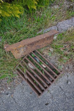 Eski, paslı bir metal ızgara, çimen ve yabani otlarla çevrili, çatlamış beton bir yüzeyde yatar. Sahne, bir ihmal duygusunu ve kentsel alanları geri alan doğayı aktarıyor..