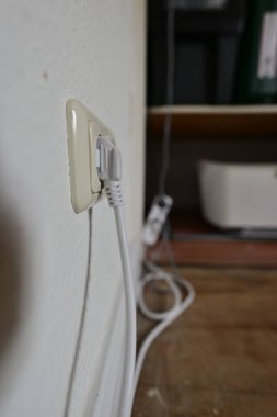 Duvardaki krikoya bağlı beyaz bir ethernet kablosunun yakın plan görüntüsü, bulanık bir arka plan, ahşap bir yüzey ve bazı elektronik cihazlar gösteriyor..