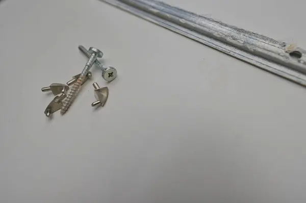 Beyaz bir yüzeyde vidalar, çapalar ve metal parmaklıklar içeren küçük donanım parçaları koleksiyonu. Eşyalar dağılmış, çeşitli şekil ve boyutlarını gösteriyor..