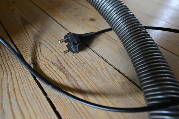 Elektrik süpürgesinin elektrik prizinin yakın plan görüntüsü ve ahşap zemindeki kablo, ahşabın dokusunu ve fişin tasarımını gösteriyor..