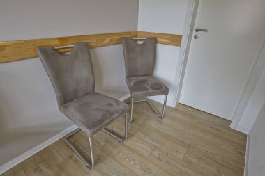 İki modern, şık sandalye, parlak bir tasarım, açık renkli bir duvara dayanıyor. Zemin ahşap ve arka planda görünür bir kapı var..