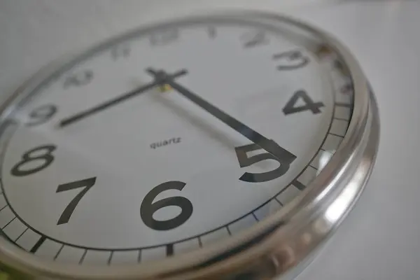 Bir kuvars duvar saatinin yakın çekimi büyük siyah sayılar ve gümüş çerçeve ile zamanı gösteriyor.