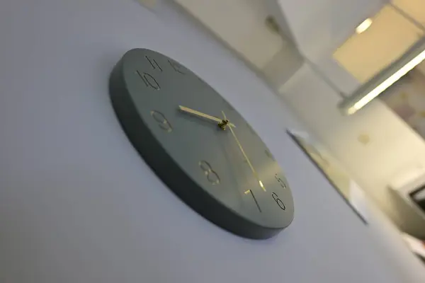 Minimalist tasarımı olan modern bir duvar saati. Açık renkli bir duvara monte edilmiş, sessiz yeşil bir yüz ve altın elli..