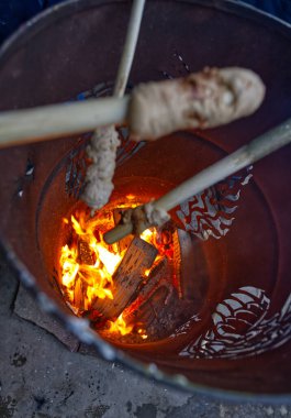 Alevlerin üzerinde hamur tutan çubuklarla bir kamp ateşinin üst görüntüsü, kızarmış ekmek..