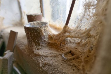 Metal borular ve aletlerle dolu tozlu, örümcek ağı kaplı bir atölyenin yakın çekimi.