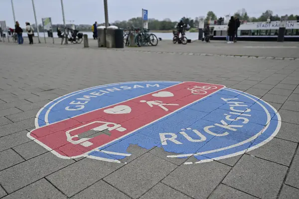 Kappeln 'de arabaların, yayaların ve bisikletlerin sembollerinin yer aldığı bir kaldırıma çizilmiş dairesel yol tabelası. İşaret, farklı yol kullanıcıları arasında paylaşılan alan ve karşılıklı saygıyı vurguluyor