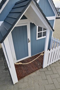 Mavi dış görünüşlü, beyaz süslemeli ve küçük ahşap verandalı büyüleyici bir oyun evi. Ev, Kappeln yakınlarındaki Olpenitz 'de bir ön kapı, bir pencere ve beyaz bir çit içeriyor.