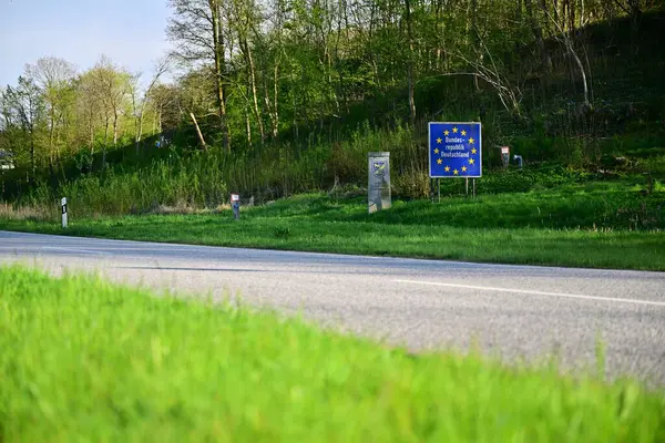 Arka planda yeşil çimenler ve ağaçlar olan bir yol manzarası. Krusa ve Flensburg 'daki Alman Danimarka sınırında Avrupa Birliği sınırını gösteren mavi bir işaret görülüyor